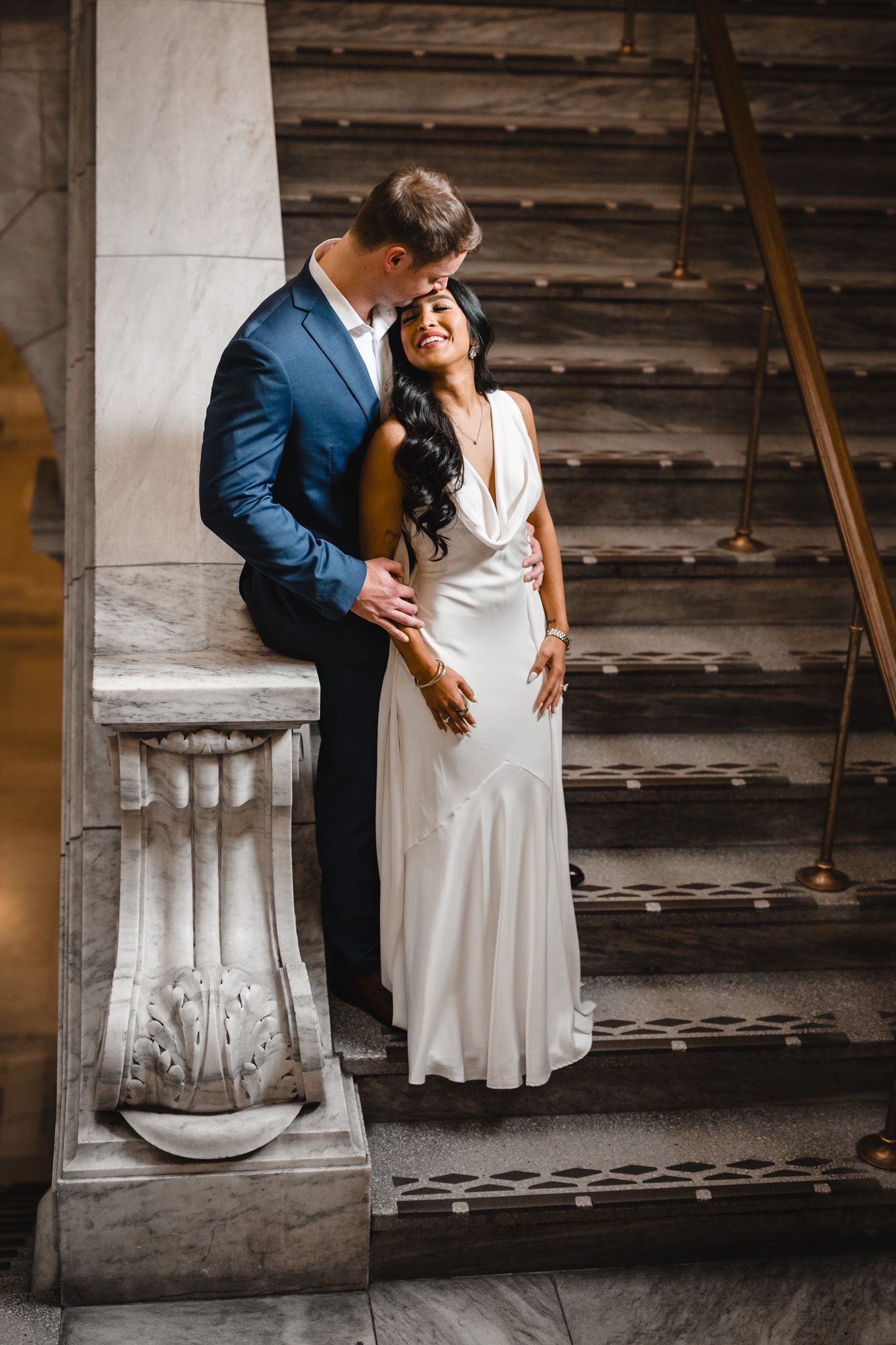 Intimate wedding moment captured against rustic wooden wall and marble architecture.