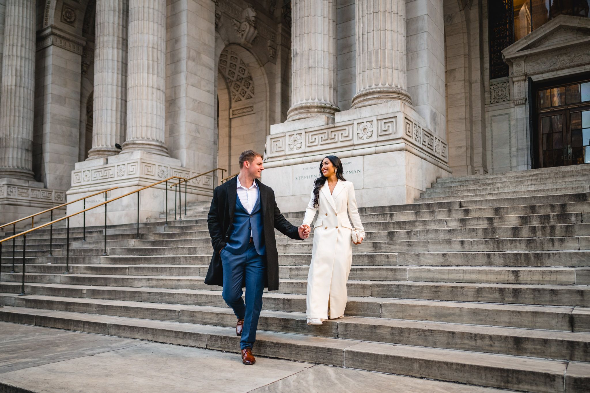 Couple walks along stone steps of historic building with classical columns.