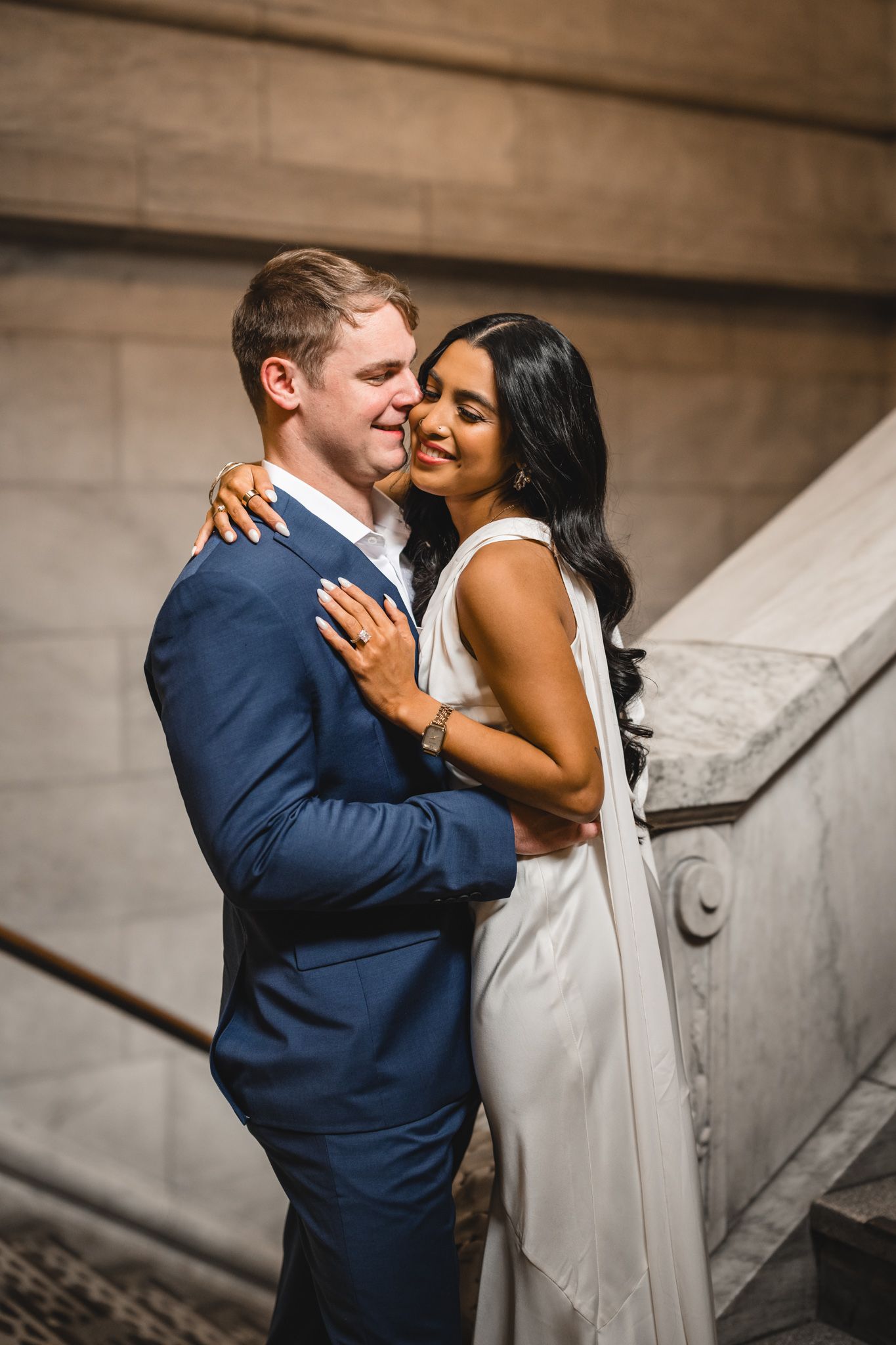Couple embraces against ornate marble balustrade in romantic wedding photo.