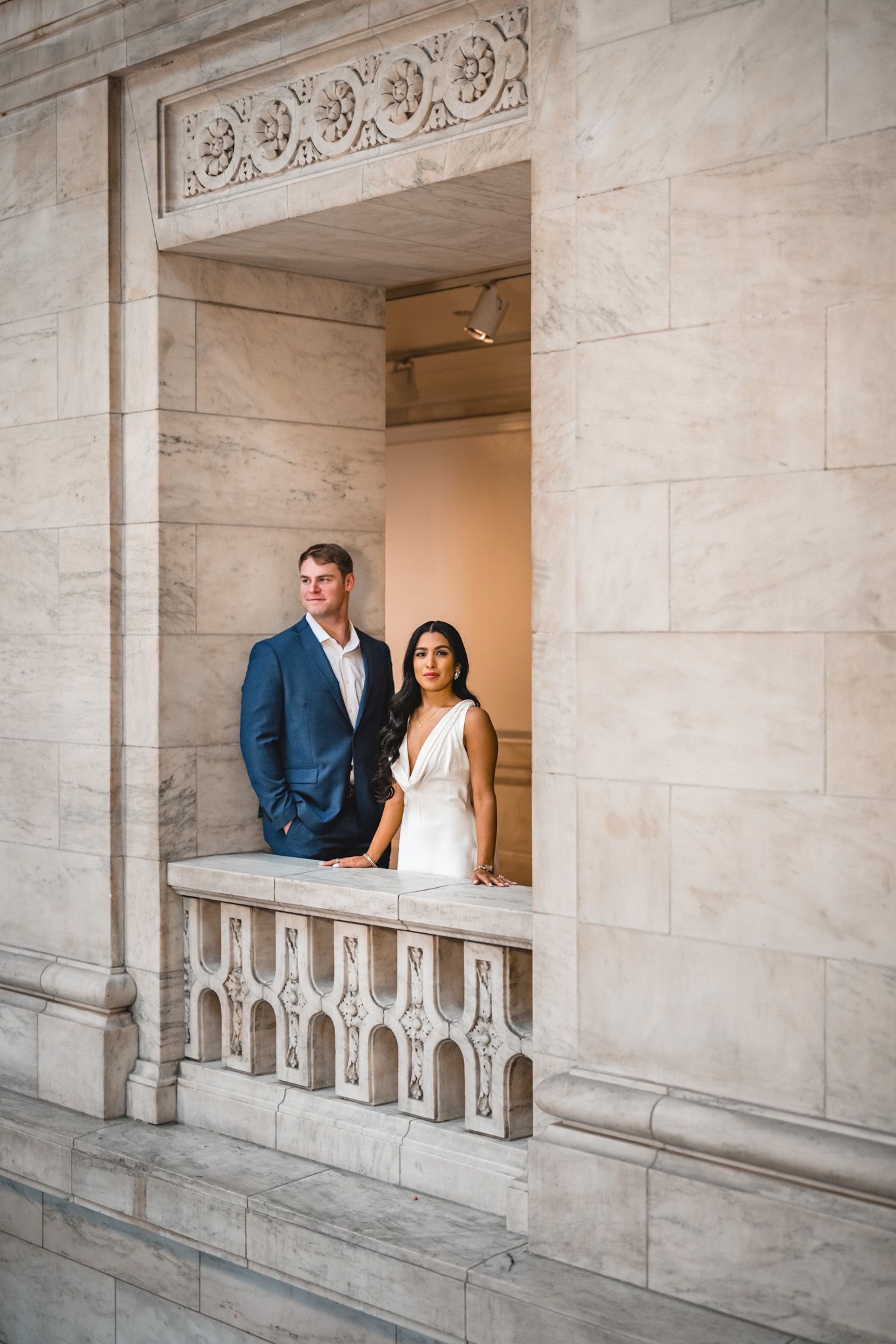 Wedding couple poses in elegant marble archway with decorative architectural details.