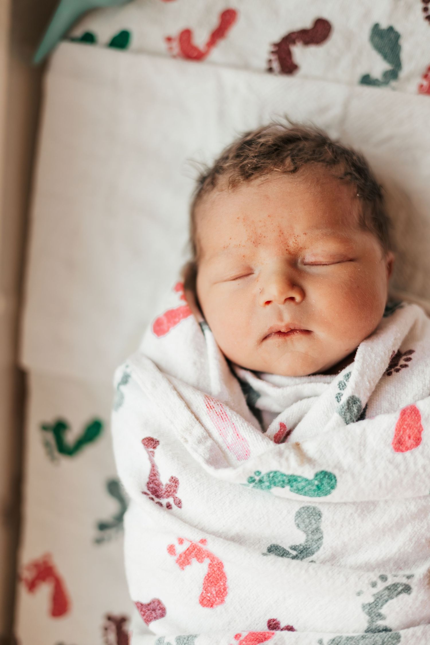 Peaceful newborn baby swaddled in a colorful footprint blanket sleeping in a hospital bassinet | Fresh 48 Hour Photos