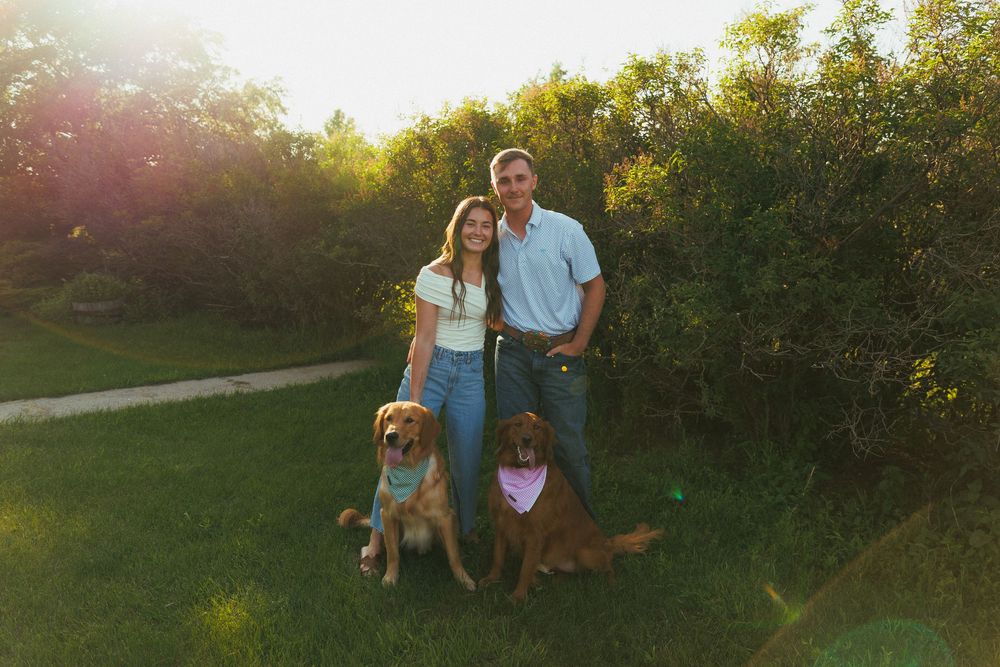 A couple poses with their two dogs on a nature path during golden hour sunset with greenery in the background.