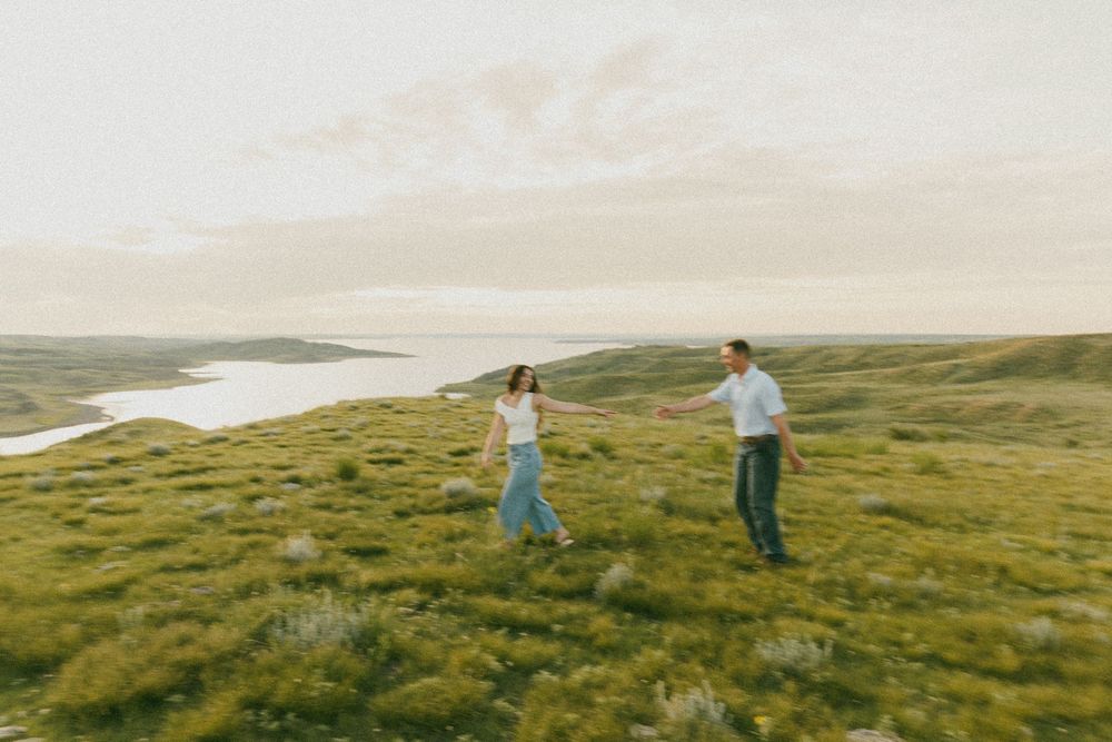 Two people walk together on a scenic green hillside overlooking a coastal landscape at sunset.