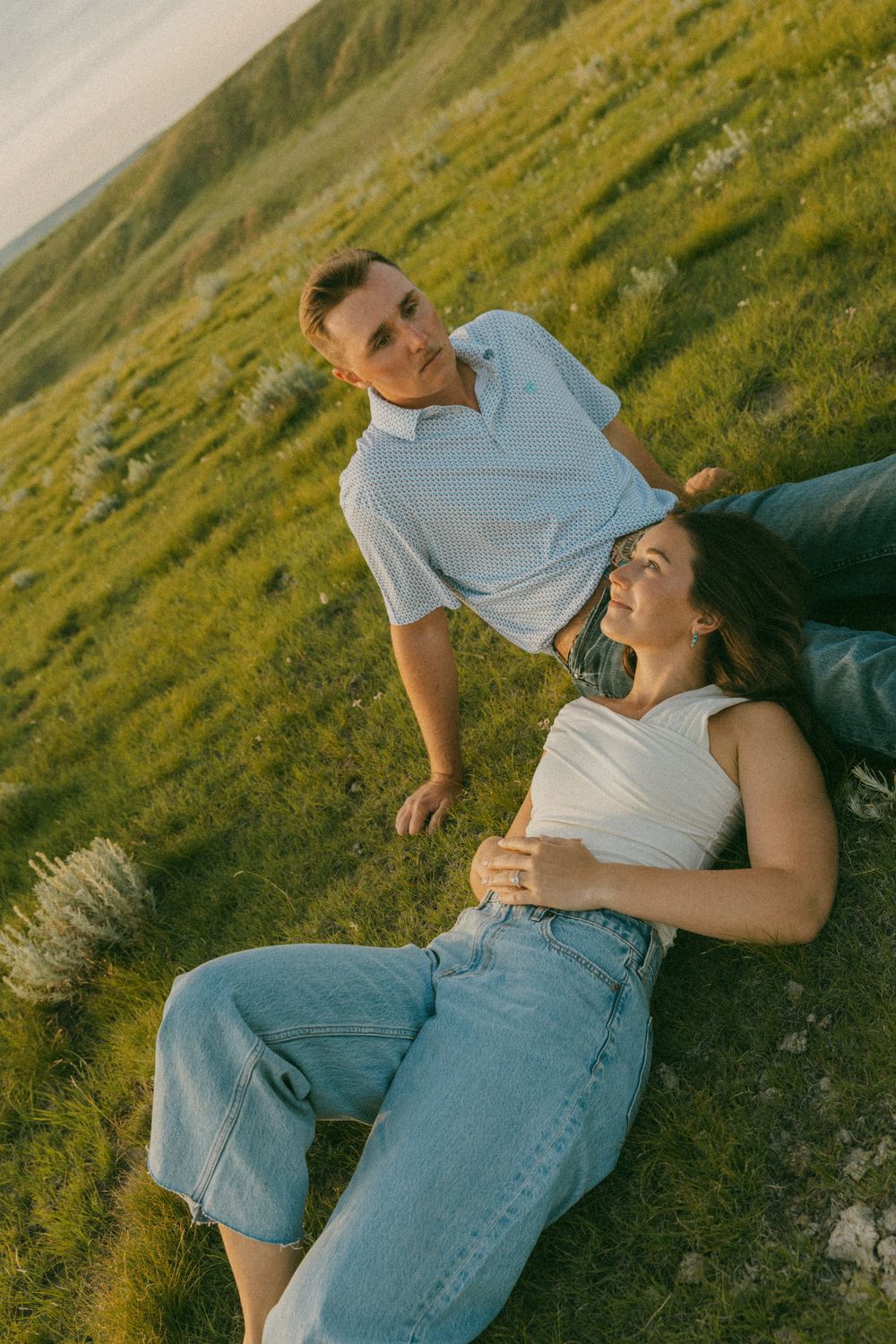 A couple lounges together on grass during a warm sunset photoshoot in nature.