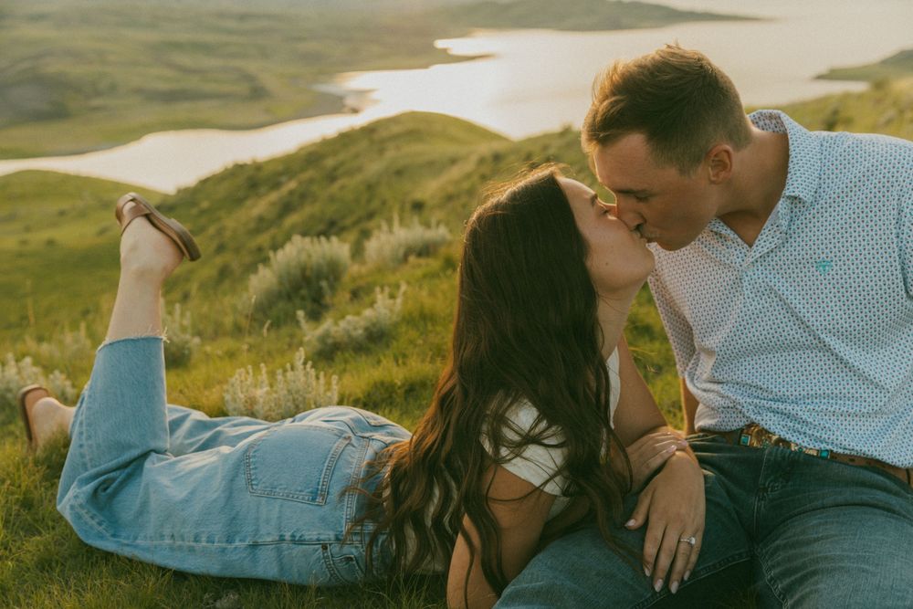 Two people share an intimate moment in a scenic mountain landscape during golden hour.