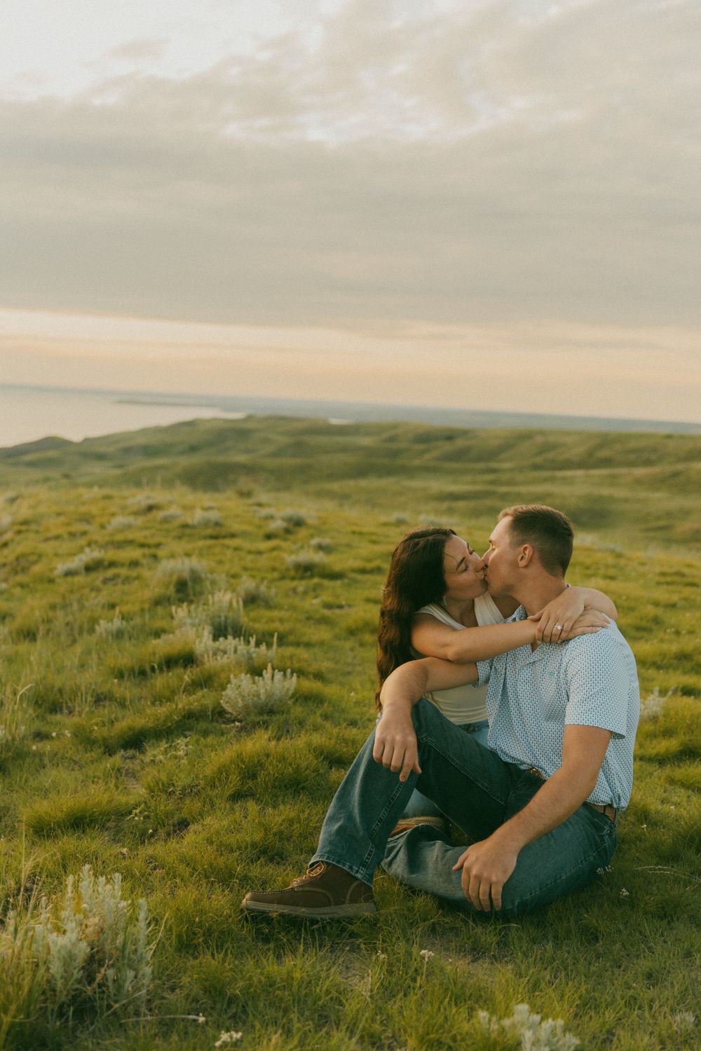 A couple shares an intimate moment while lying in a green meadow during golden hour.