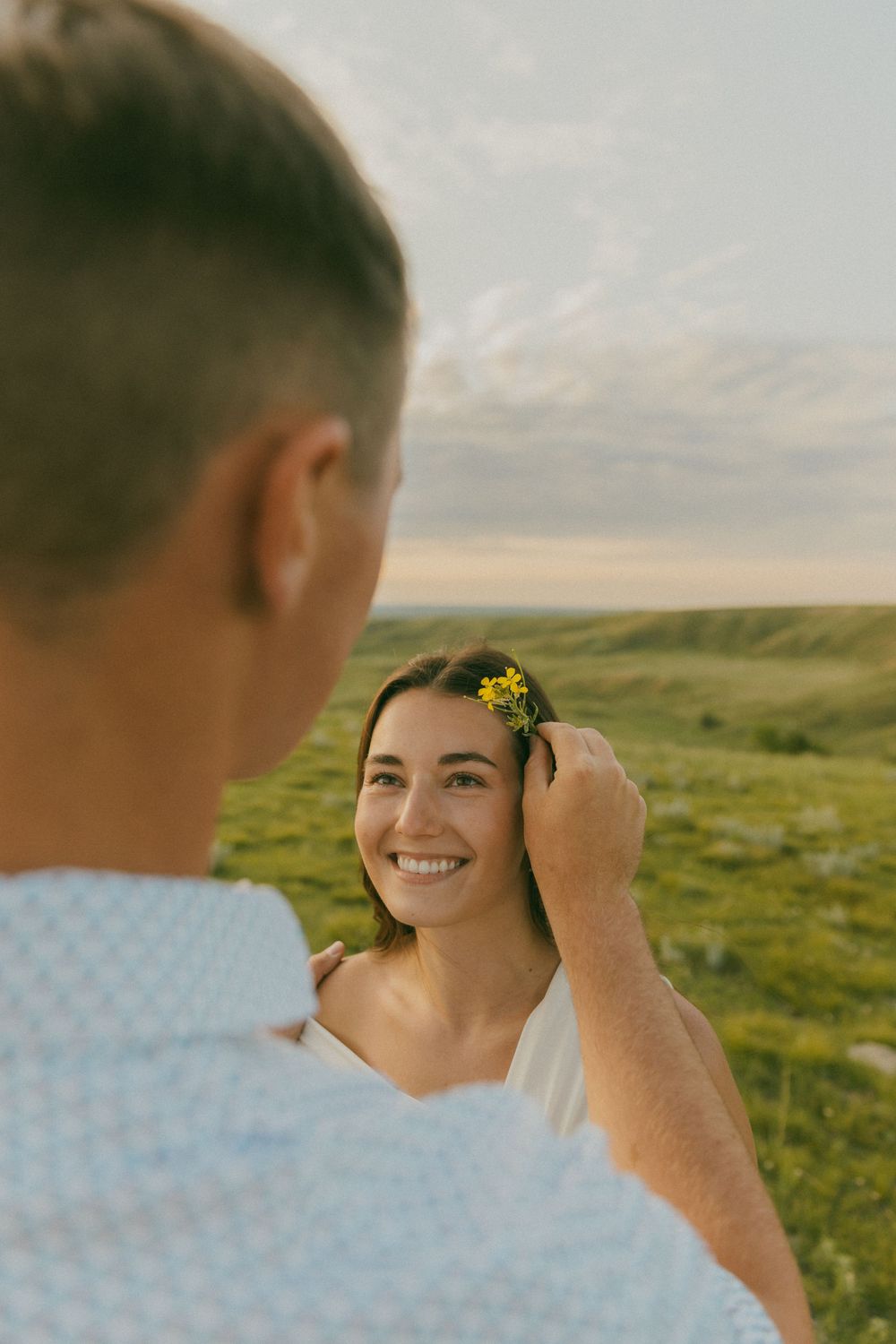 A gentle moment captured in nature as a yellow flower is placed in hair against green rolling hills.