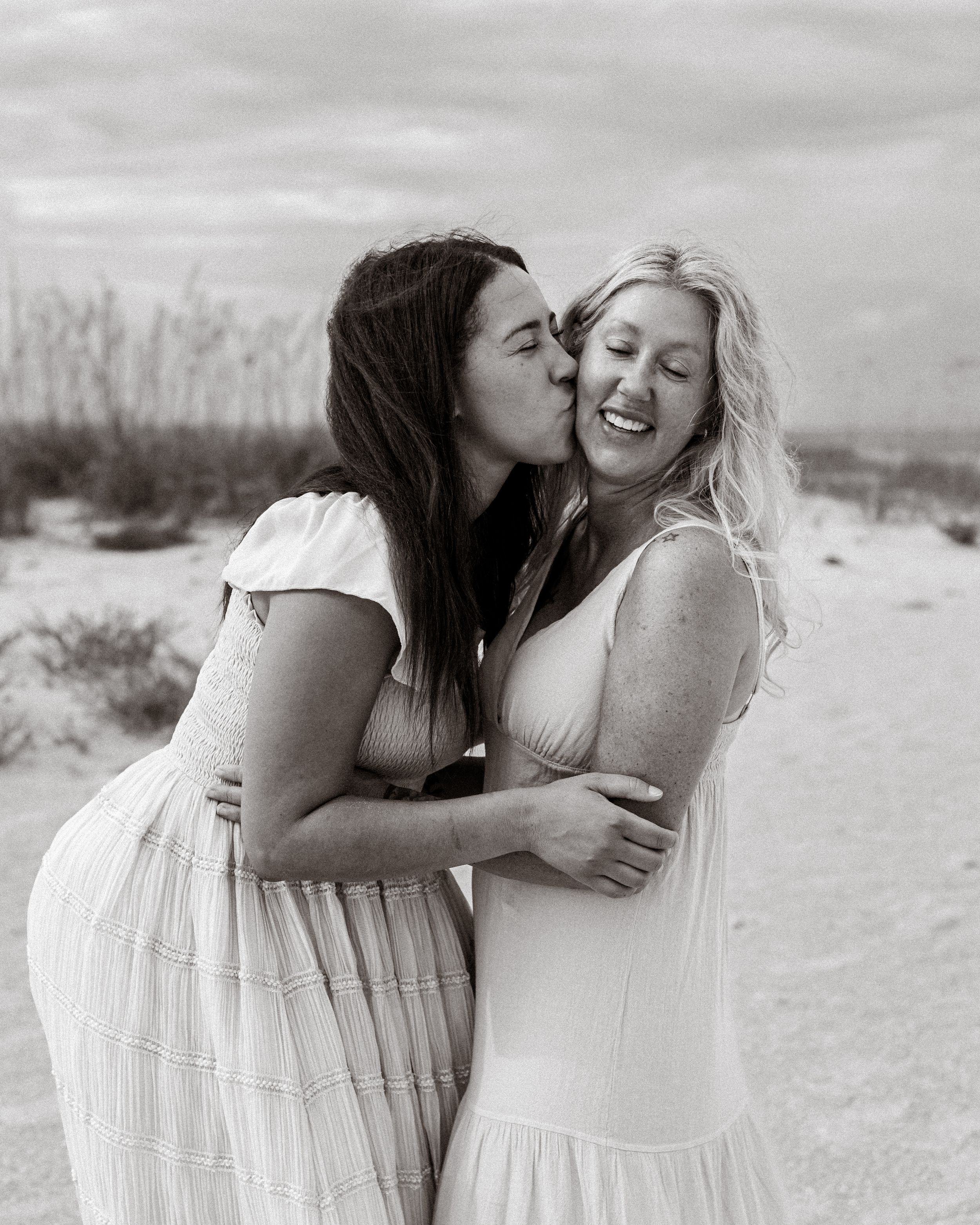 Daughter kissing mother's cheek during a family portrait session on the beach in St. Petersburg, Florida.