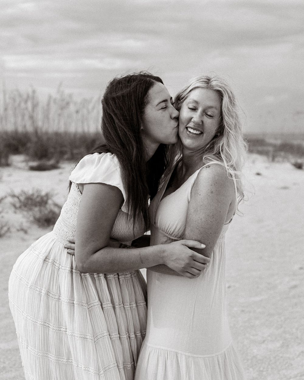 Daughter kissing mother's cheek during a family portrait session on the beach in St. Petersburg, Florida.