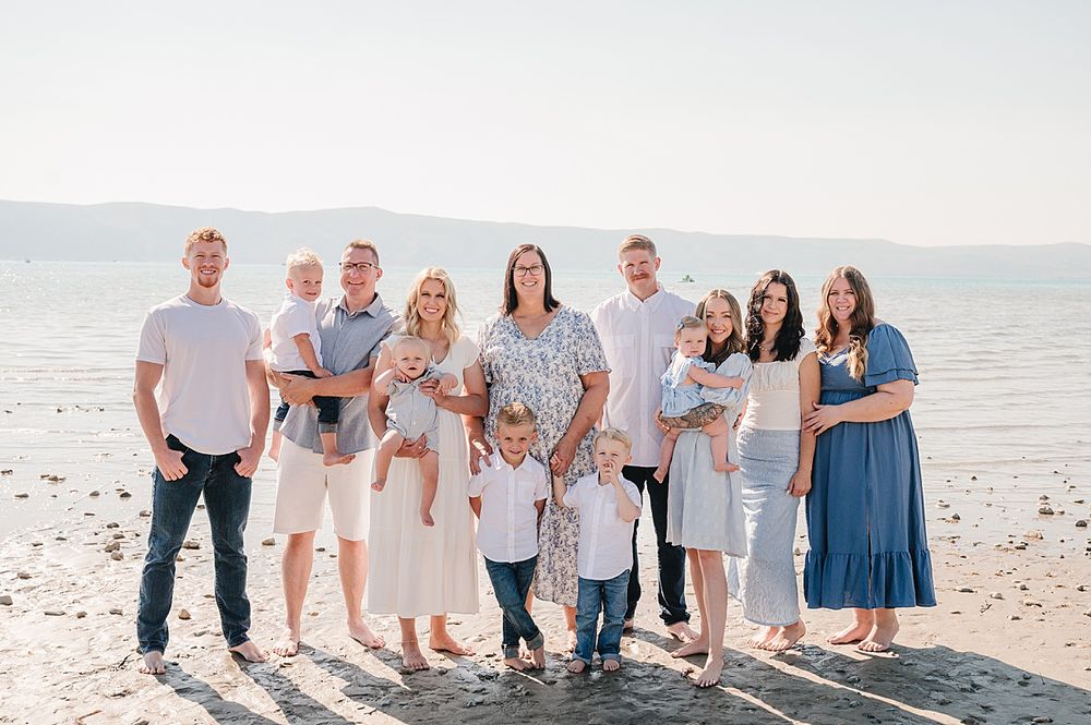 A group of people wearing coordinated white and blue outfits pose together on a sunny beach at sunset.