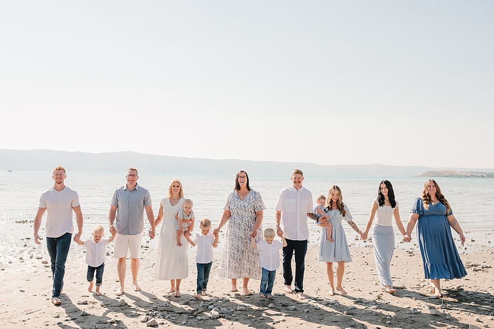 A group in coordinated white and blue outfits walks together on a sunny beach with mountains visible in the distance.