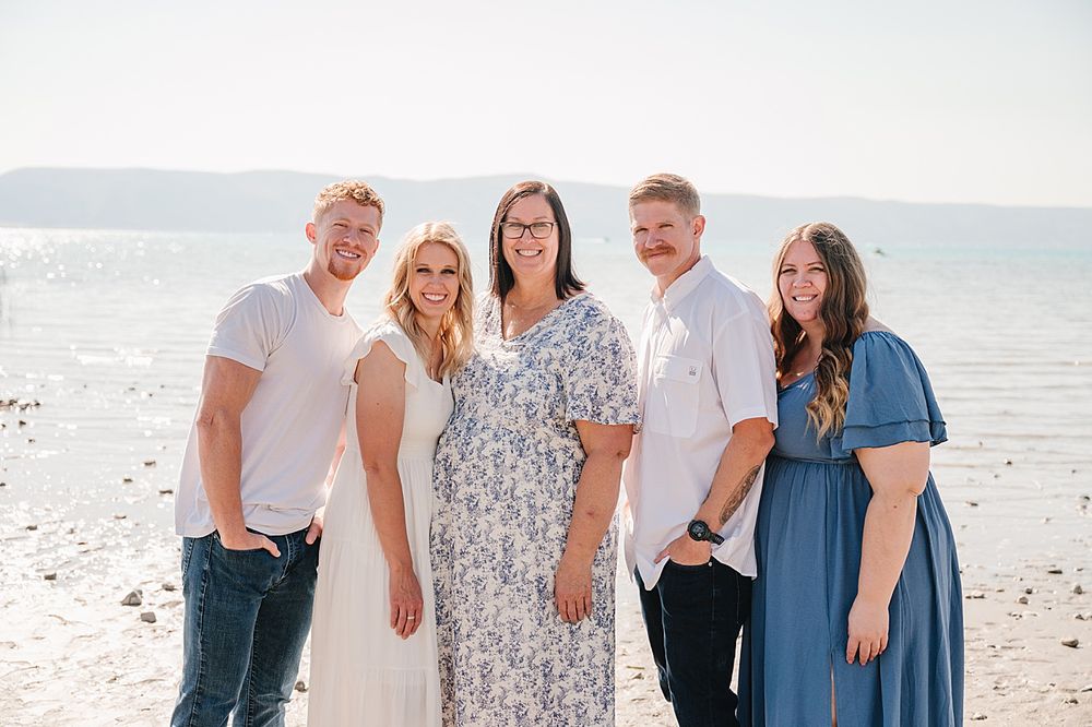 A group in coordinated blue and white outfits smiles together on a sunny beach during a photo session.