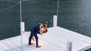 A person walking along a white wooden dock over calm blue water, creating a serene lakeside scene.