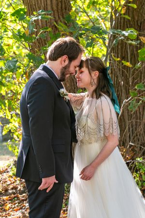 A romantic wedding couple shares intimate moments under sunlit trees during an outdoor autumn ceremony.