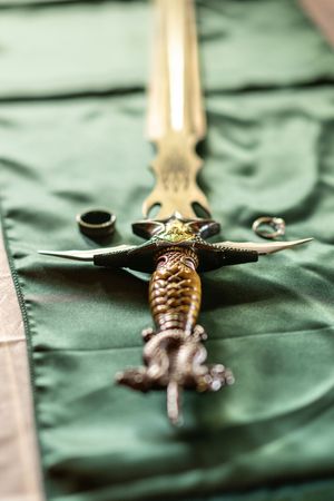 Close-up of an ornate antique dagger handle with decorative metalwork against a green fabric background.