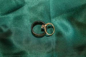 Two wedding rings, one gold and one black, rest on an emerald green satin fabric surface.