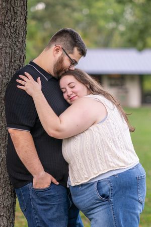 A tender romantic moment shared between a couple embracing outdoors near a tree on a sunny day.