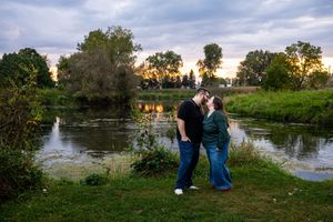 Couple enjoying a peaceful sunset moment by a serene pond surrounded by lush greenery and trees.
