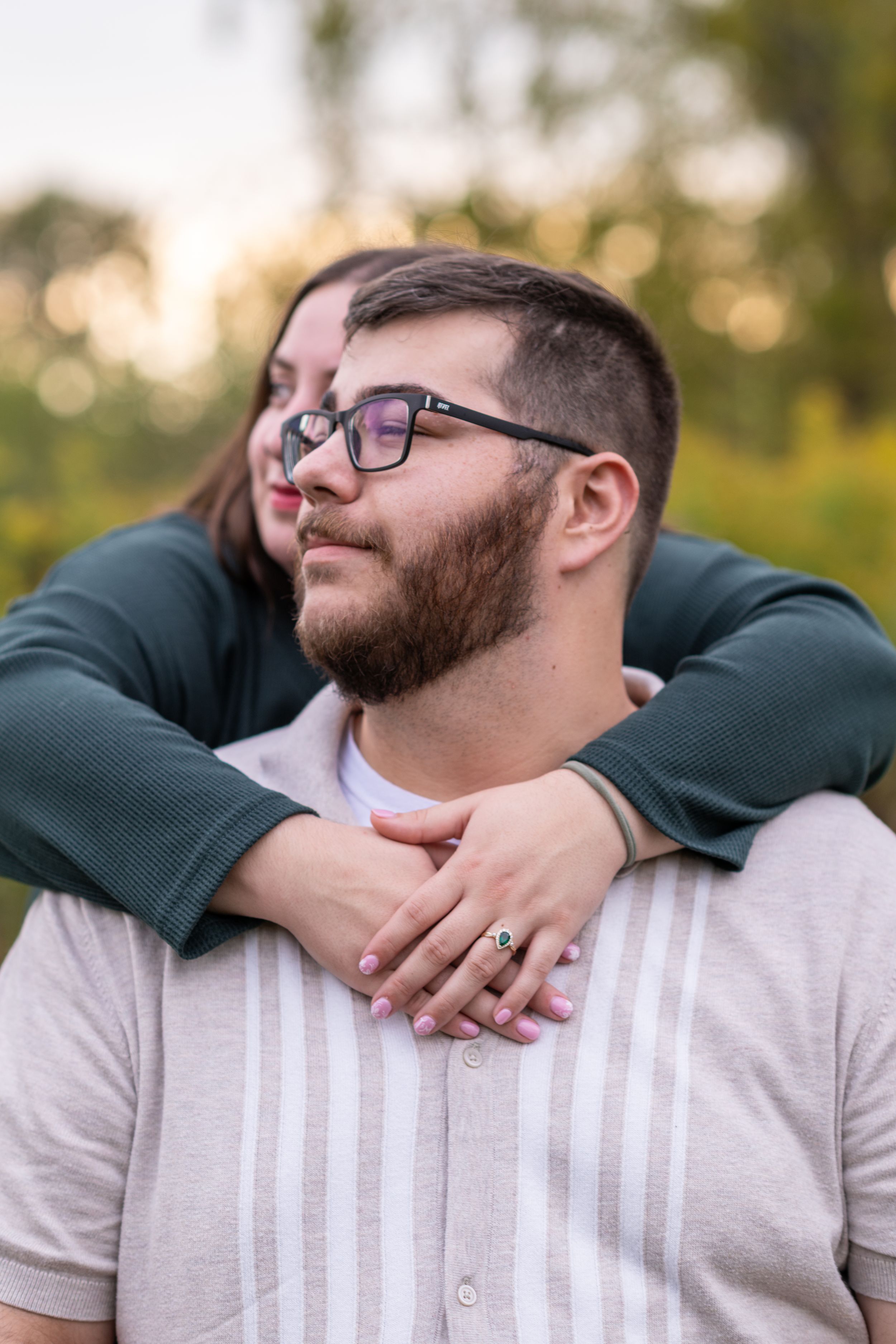 A couple embraces in a romantic outdoor setting during golden hour, wearing casual attire.