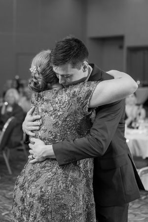 Groom and mother share emotional dance embrace at wedding reception in black and white photo.