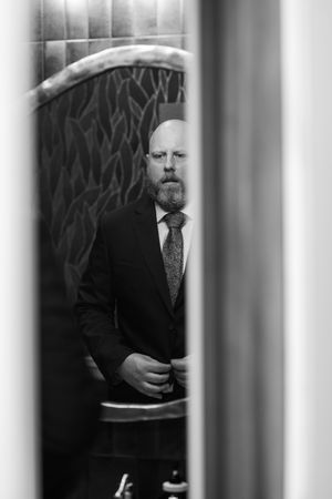 Black and white portrait of a bearded man in a suit and tie, reflected in a mirror.