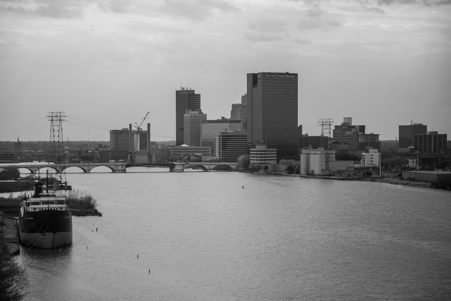Grayscale urban skyline with industrial buildings reflected in river waters.