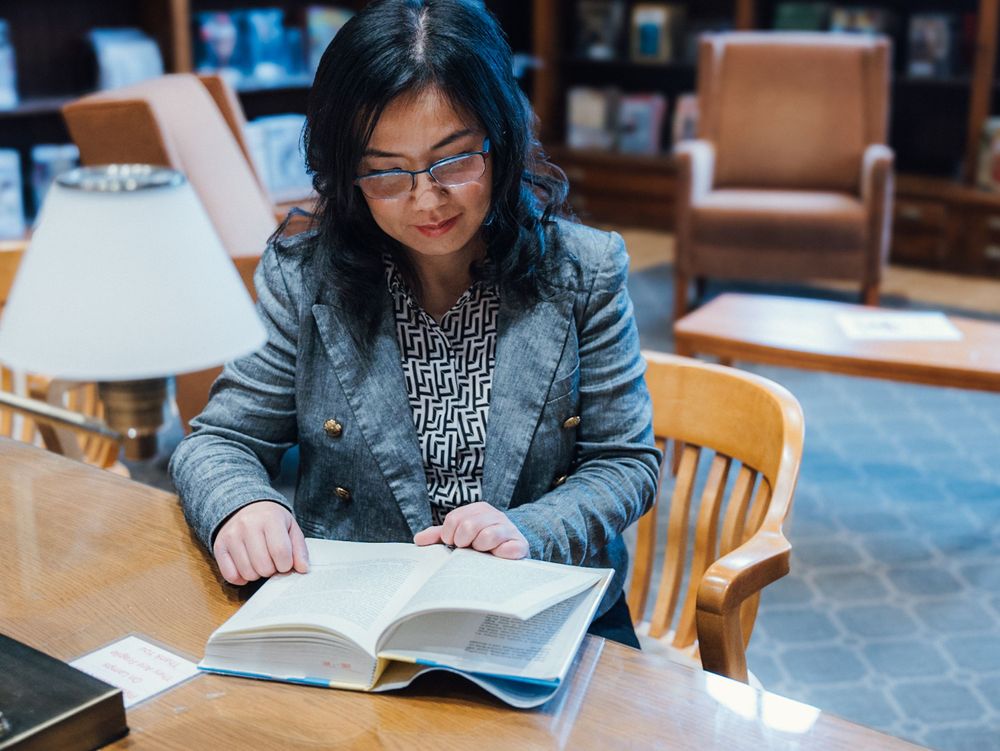 A person studies at a wooden table in a library environment.