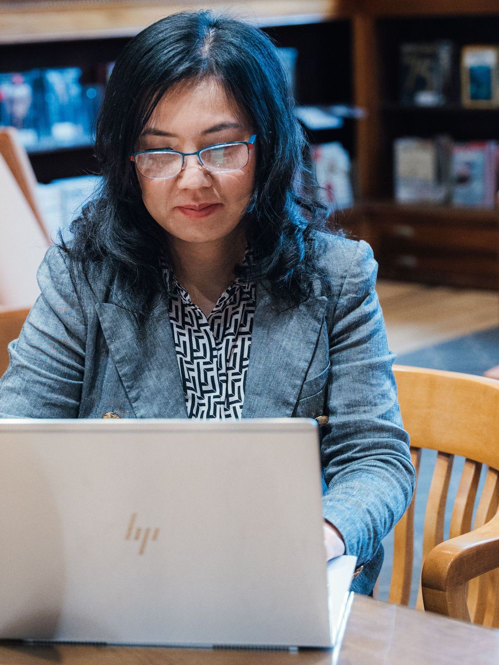 Someone works on a laptop while seated at a wooden desk in a library.