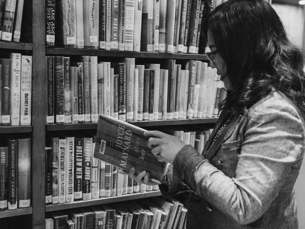 A person browsing books on library shelves in dim lighting.