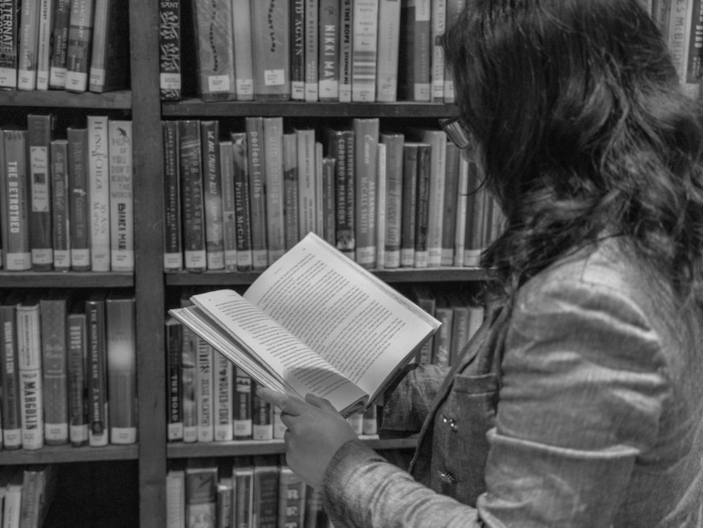 A person browses books in a library surrounded by floor-to-ceiling bookshelves in a black and white photo.