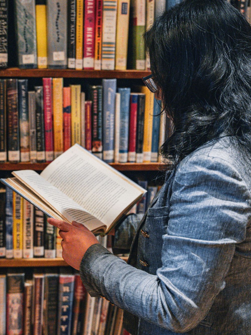 Someone reading a book while standing between library shelves filled with colorful books.