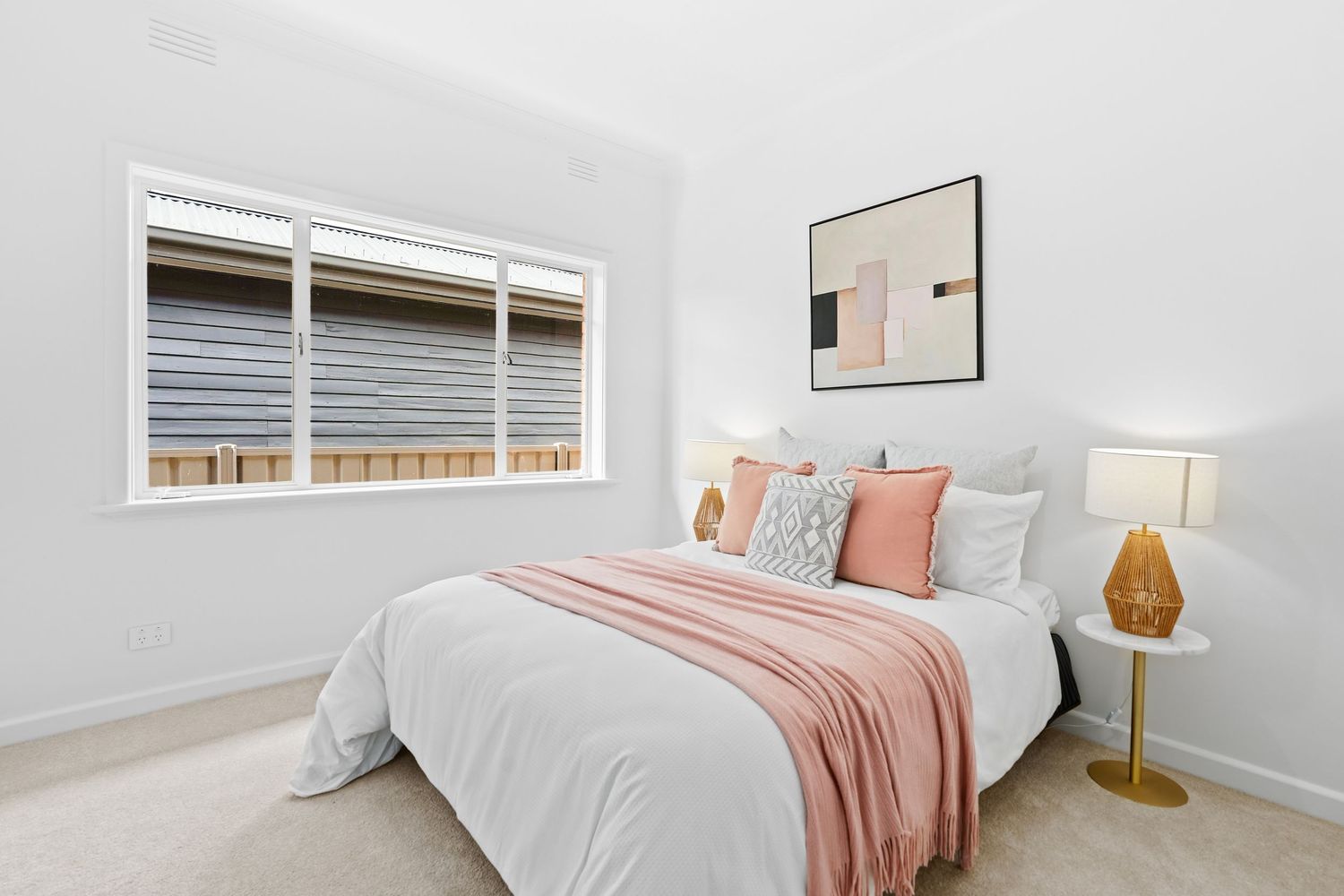 Modern bedroom with pink accents, white bedding and gold table lamp.