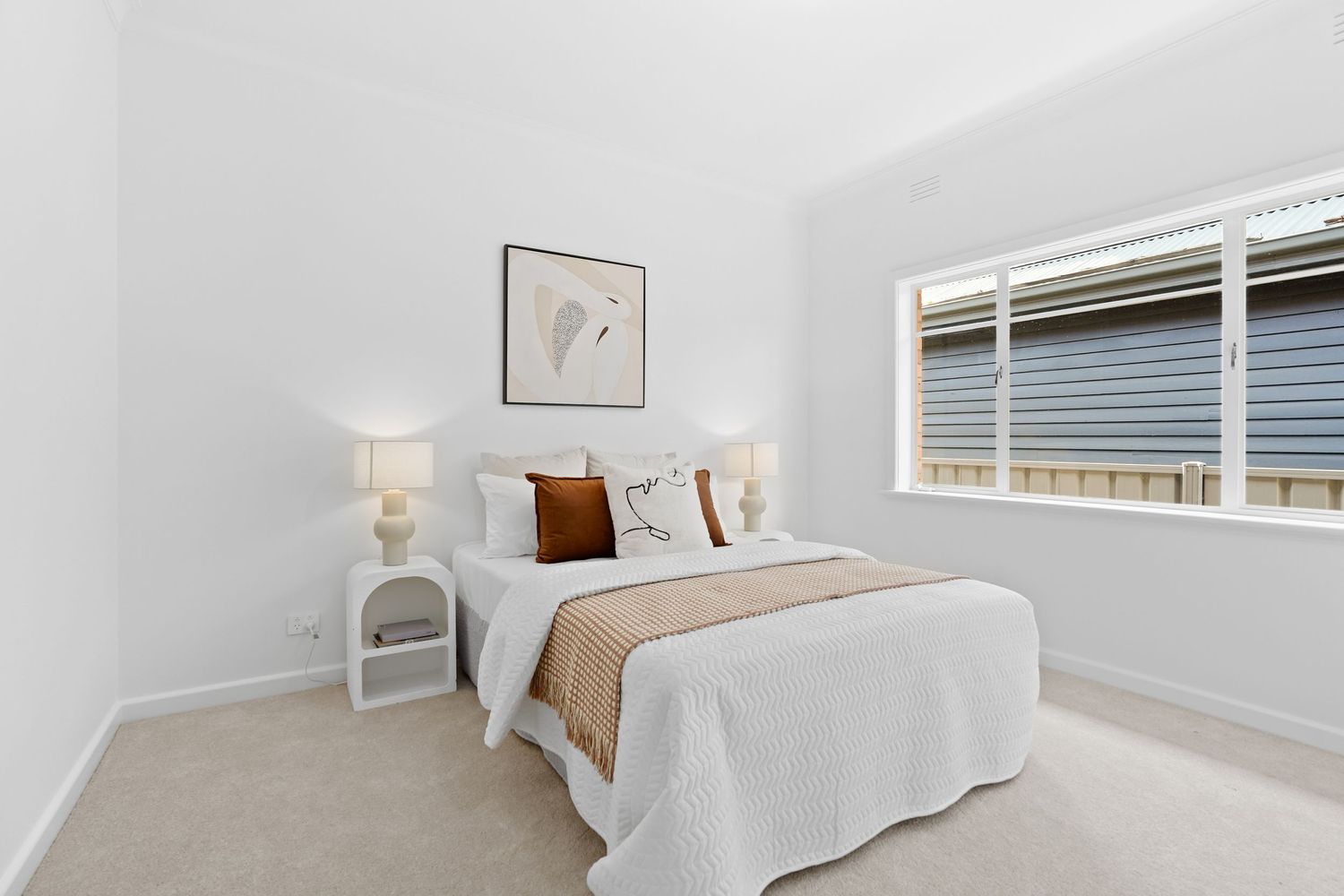 Minimalist bedroom with beige accents and natural light from window.