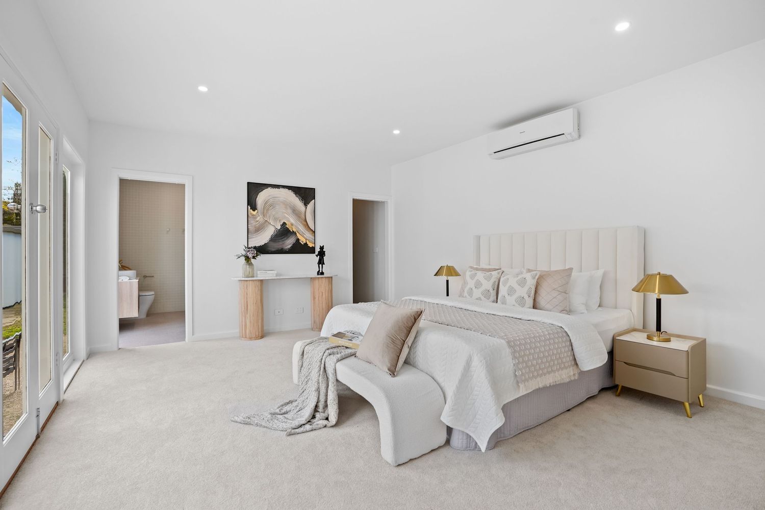 Contemporary master bedroom with beige textiles and large windows letting in natural light.
