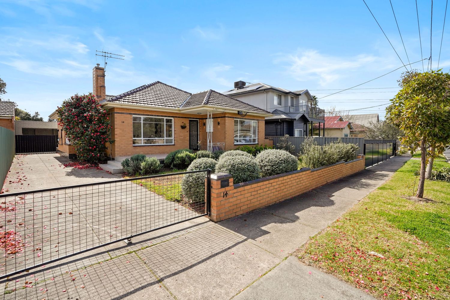 Single-story beige brick house with front garden and driveway gate.