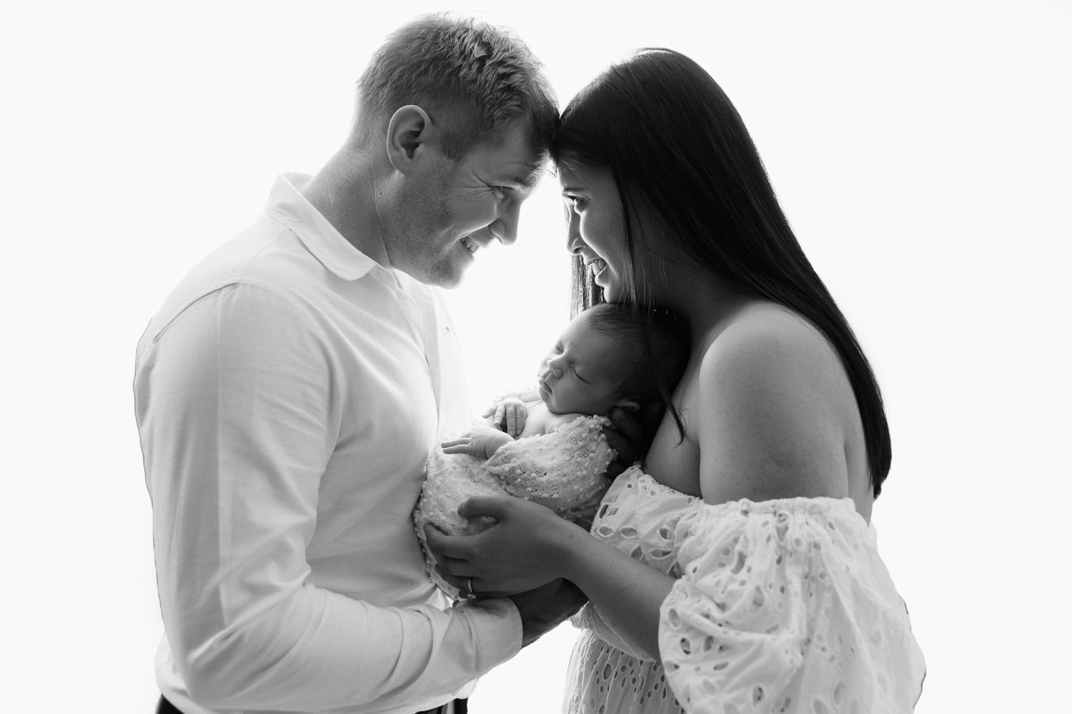 Silhouette of new parents lovingly gazing upon each other with their newborn baby cradled between them