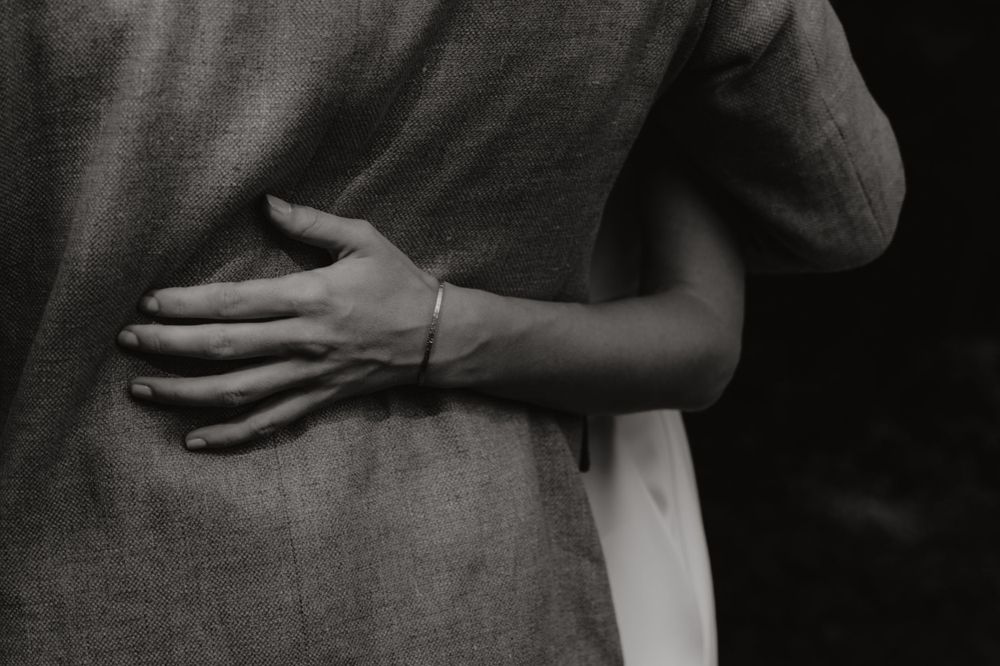 A black and white close-up photograph showing hands embracing in an intimate romantic gesture.