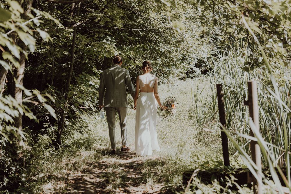 A romantic wedding couple walking down a sunlit forest path together.