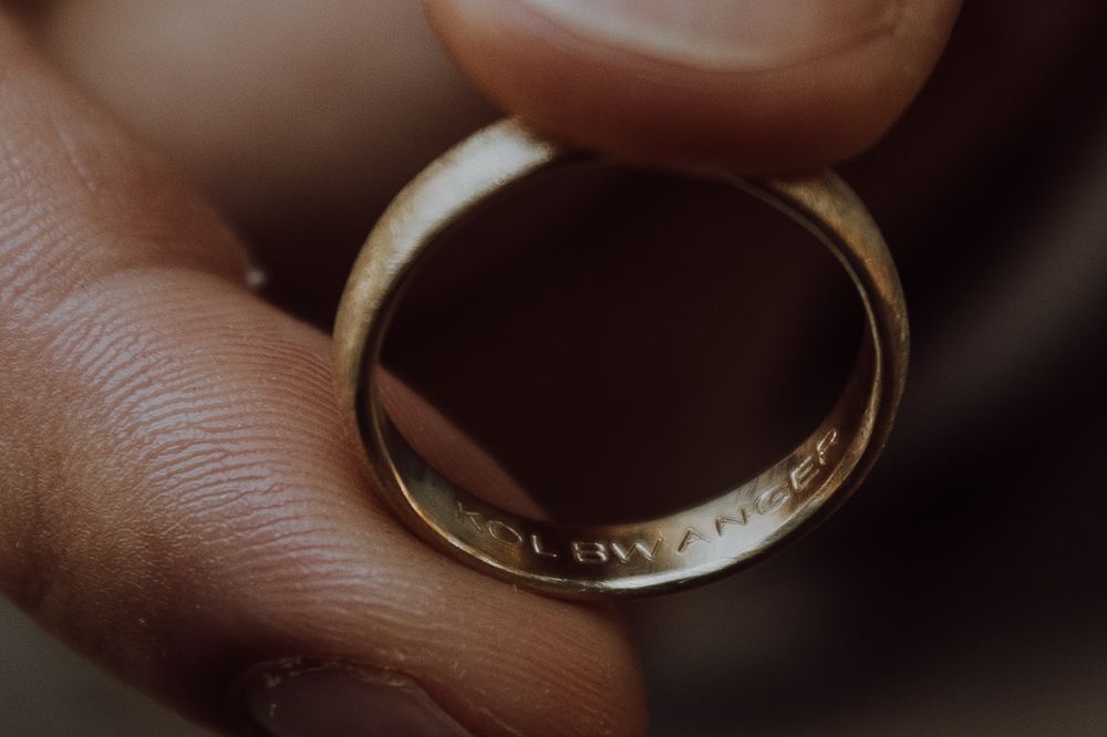 Macro shot of a gold wedding ring held between fingers showing intricate details.