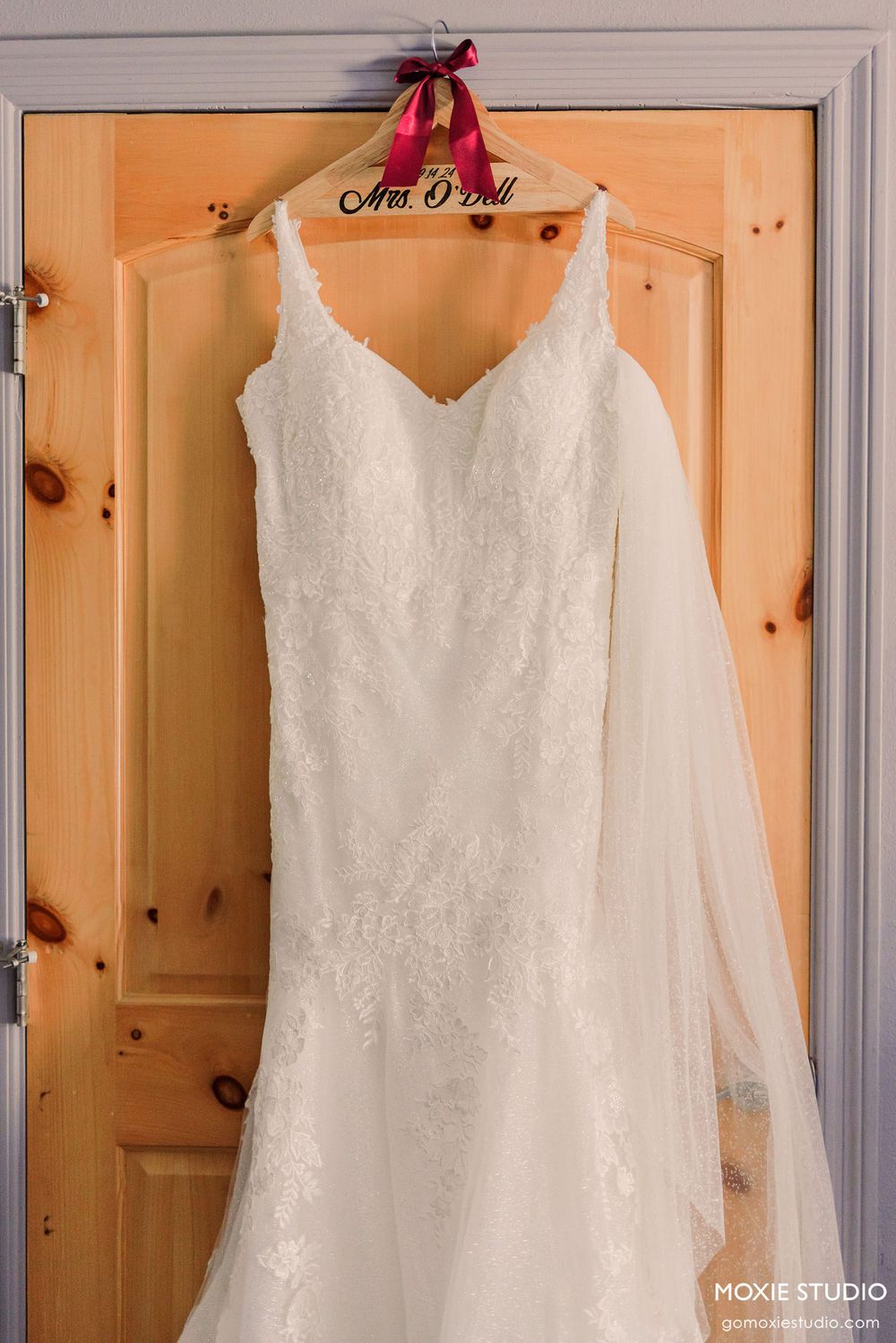 Three elegant white lace wedding dresses hanging on wooden hangers against a cream-colored wall.
