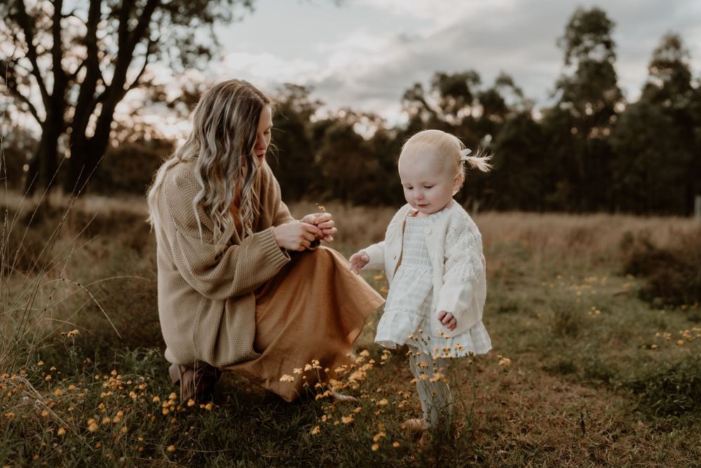 Mother kneeling in wildflower field, smiling at toddler daughter taking steps toward her.