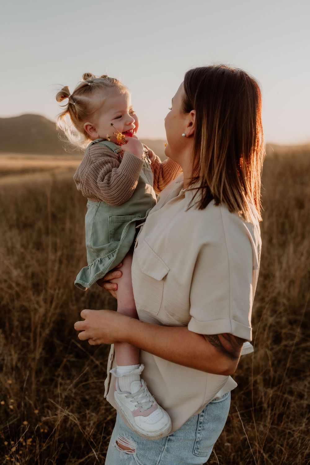 A brunette mother holds her baby girl up close in a sun-drenched golden field.