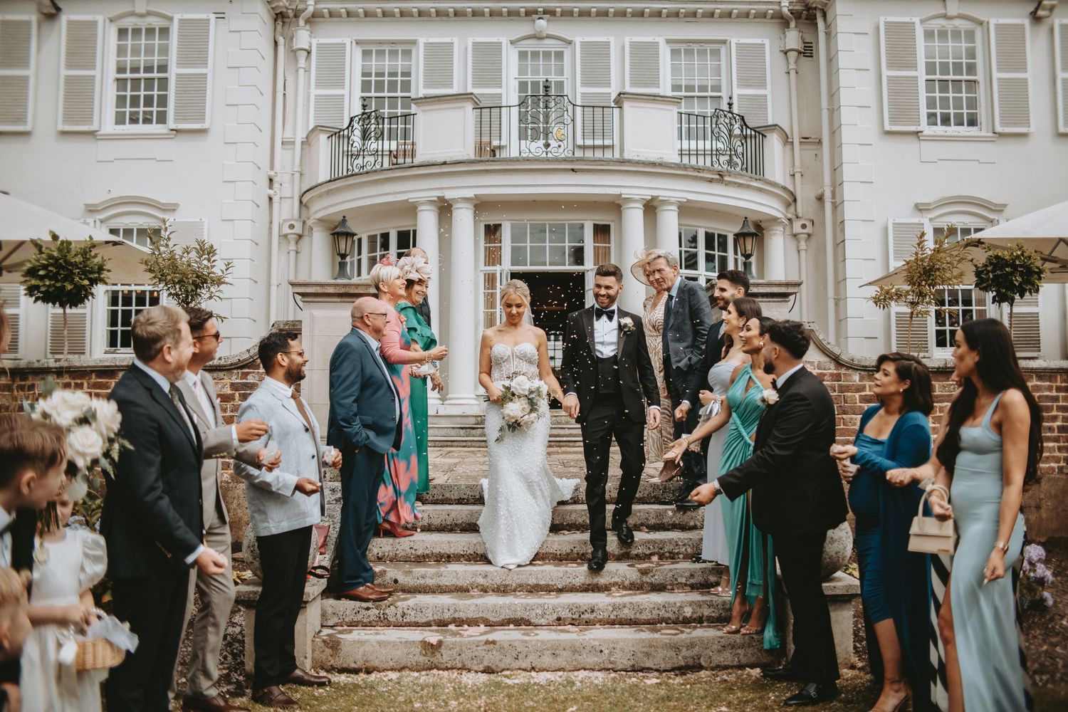 Wedding guests line up outside a grand white mansion for a celebration.