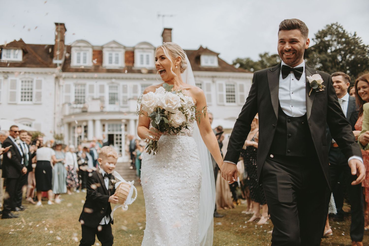 Joyful wedding celebration with guests throwing confetti in front of a historic building.