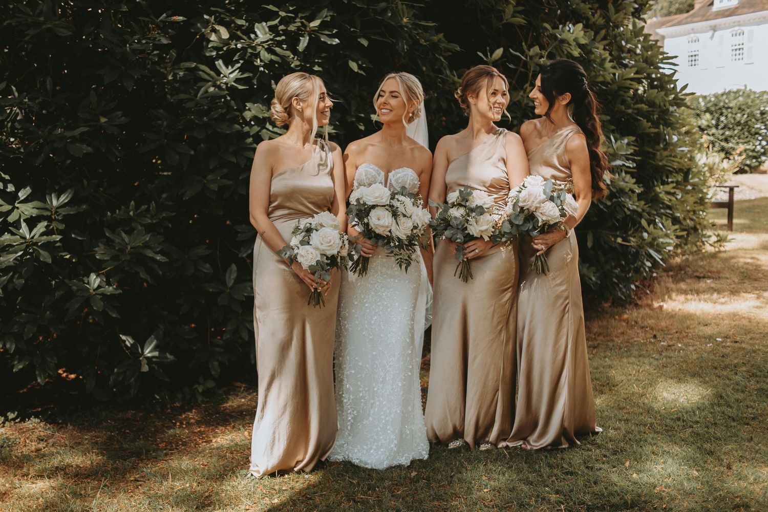 Bridal party in neutral-colored dresses poses together outdoors.