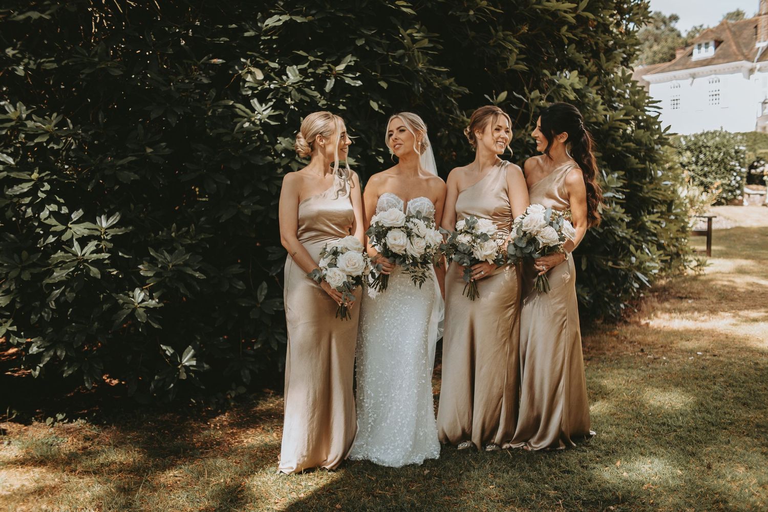 Wedding party members in champagne-colored dresses gather for outdoor photos.