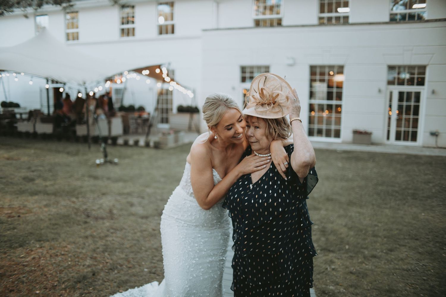 Wedding party poses outside a white building with windows during celebration.