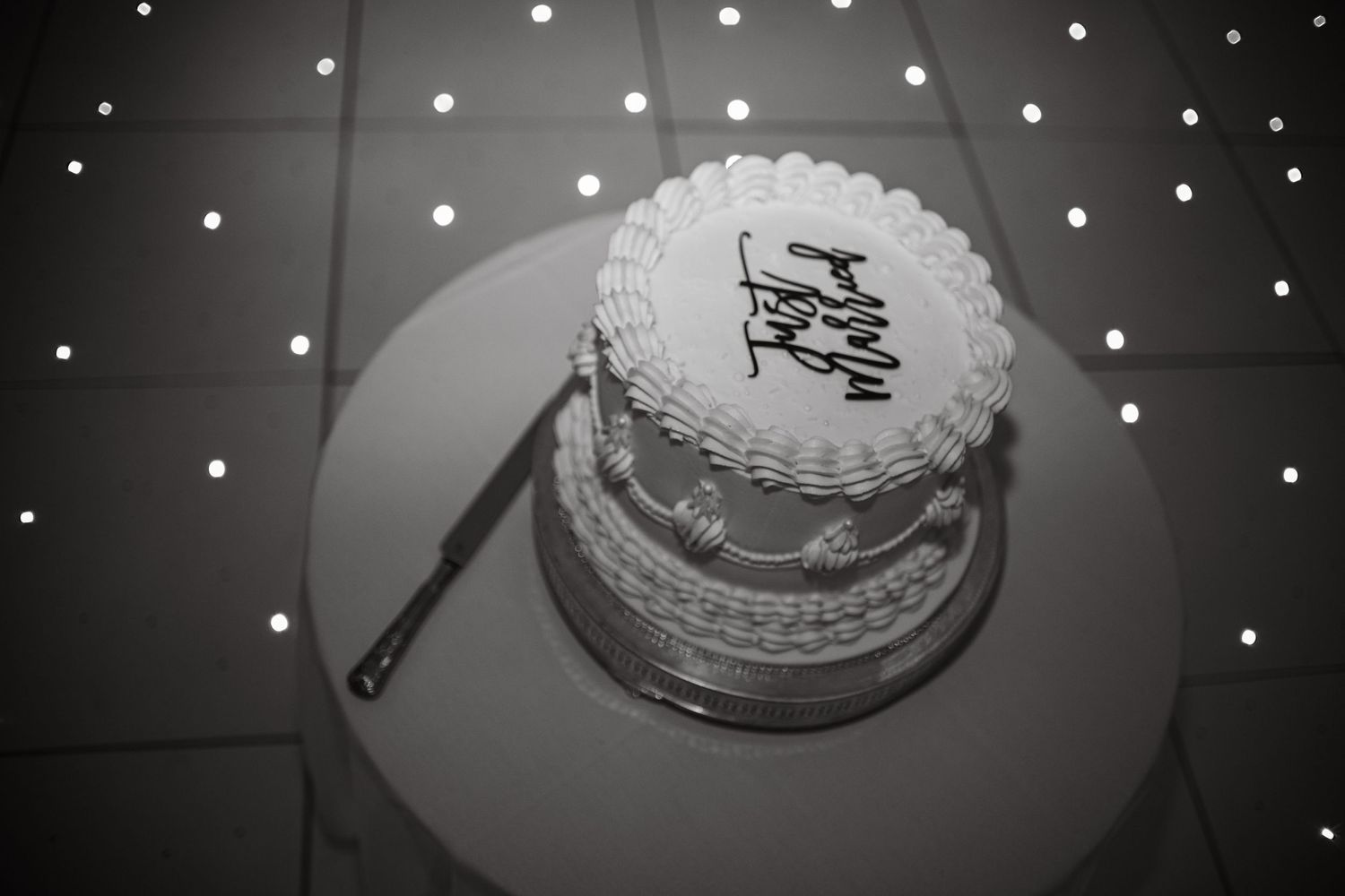 Decorative string lights twinkle above an elegant wedding cake display at a reception.