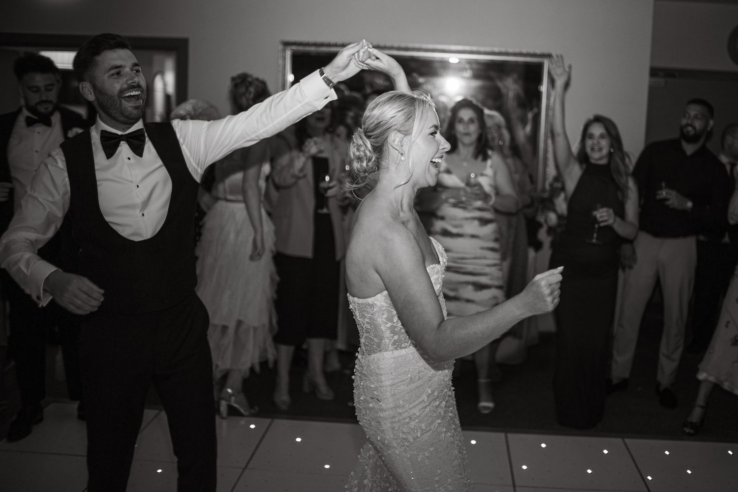 Couples dance together on an illuminated dance floor during an evening wedding reception.