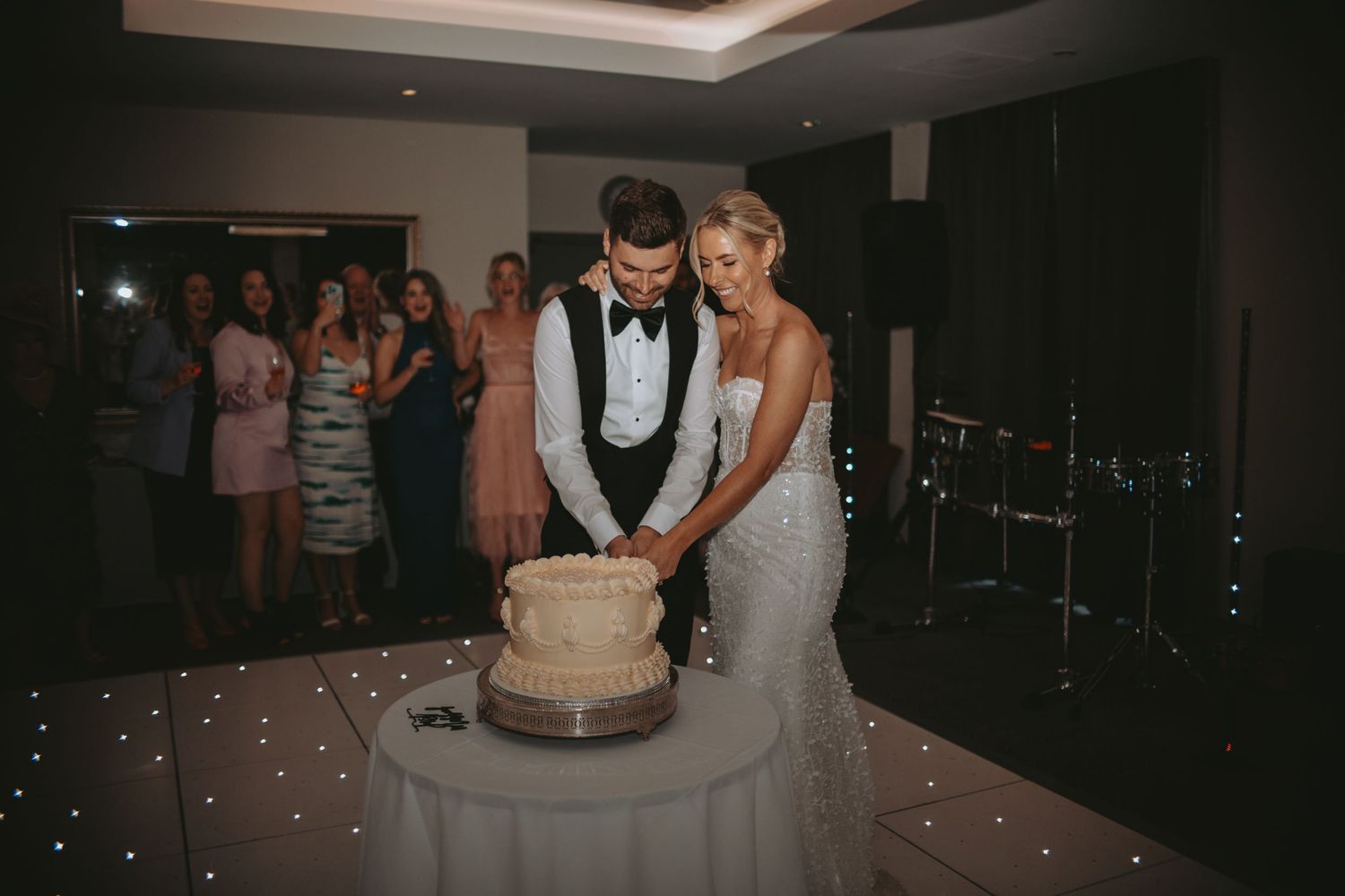 A couple shares their first dance on an illuminated dance floor surrounded by wedding guests.